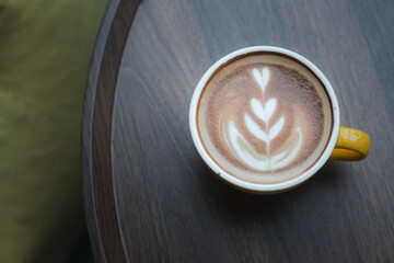 Close-up of hot cappuccino with beautiful latte art in yellow ceramic cup on wooden table.
