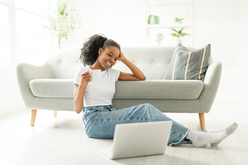 Young woman sitting on floor by the couch using laptop. Afemale working on laptop computer at home.