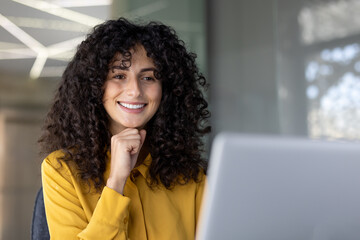 A beautiful woman smiles as she works on a laptop, looking cheerful and content, enjoying a moment of productivity.