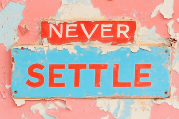 A colorful wall features a weathered sign that reads never settle, encouraging passersby to embrace ambition and perseverance in life