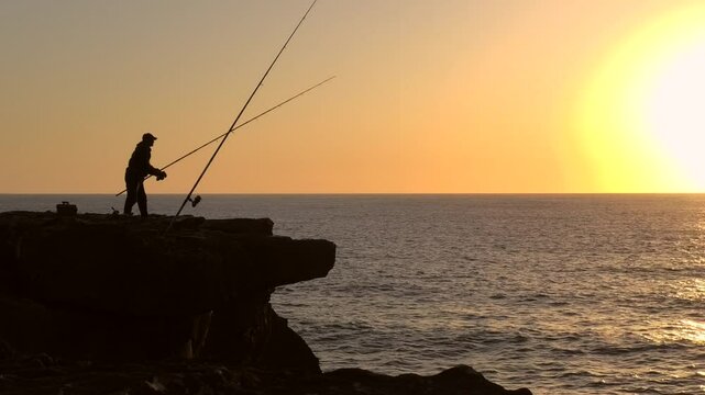 Angler wirft bei Sonnenuntergang an der Meeresk&uuml;ste die Angel aus, Gegenlicht