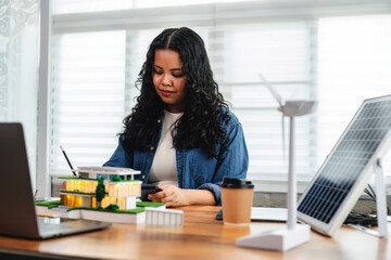 Female engineering student uses calculator and takes notes on eco-home design with solar panels and wind turbines, sustainable development, and clean energy planning.