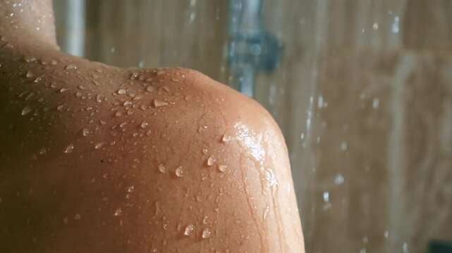 Close-up: Water droplets running down bare skin on shoulder during shower.Woman's shoulder under running shower water. Hygiene and body care concept.Relaxation.