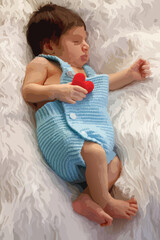 Cute baby boy sleep on white fluffy blanket and hold a little red heart in his hand. Love and health care concept. Image trace vector. 
