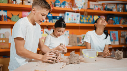 Smart highschool student using hand to press on clay piece at pottery workshop. Group of happy...