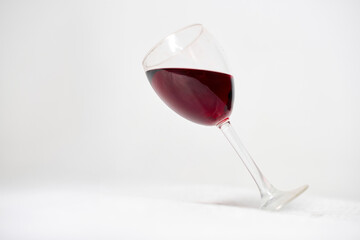 Tilted wine glass filled with red wine rests against stark white background. Minimalistic setup emphasizes rich color contrast between wine and setting, creating serene yet dynamic composition