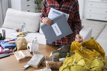 Survival kit. Woman holding documents near table with different emergency supplies indoors, closeup