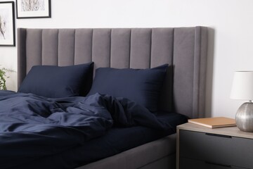 Bed with beautiful dark blue silk linens and nightstand at home