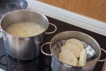 Czech leavened dumplings are heated in a steamer and a pot of cabbage is on the stove next to them