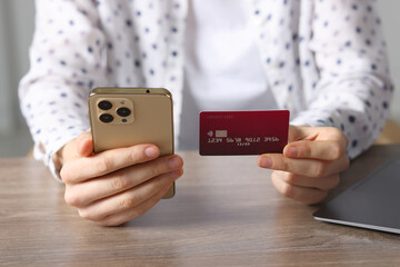 Woman with credit card and smartphone paying online at wooden table, closeup