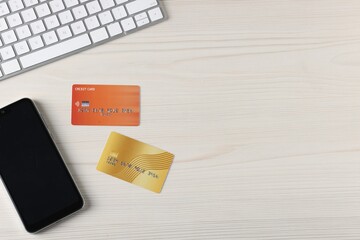 Online payment. Credit cards, smartphone and computer keyboard on light wooden table, flat lay. Space for text