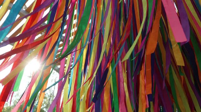Ends of colorful hanging ribbons sway in wind in sunlight. Decorative abstract composition in park from many ribbons on day of summer solstice.