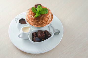 Delicious Korean Bingsu shaved ice dessert with chocolate brownie pieces, chocolate sauce, and condensed milk on a white plate, Sweet Indulgence.
