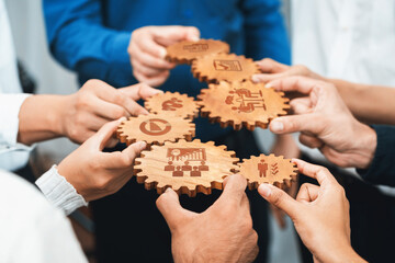 A diverse group of hands holds wooden gears, each representing different aspects of teamwork and...