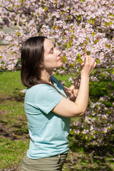 Obraz premium Portrait of a young woman admiring blooming sakura in a sunny spring park