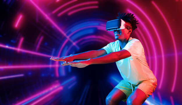 African man wearing VR headset while exercising at an abstract background with glowing pink and blue color. Attractive male model playing fitness while wearing white shirt. Technology. Ingenuity.