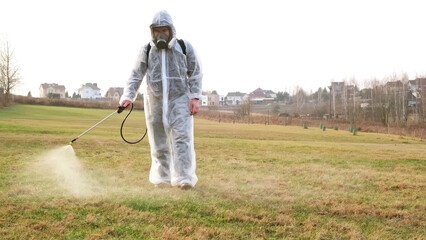 Man wearing protective suit treats the lawn from insect parasites using poison sprayer. Weedkiller....