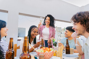 At a gathering of friends with food, young Latin men and women hold glass cups for a toast