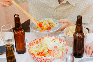 Unrecognizable young man, at shared lunch, with bottles of beer, serves salad on a plate