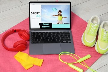 Laptop with sport blog web site and different gym stuff on floor, above view