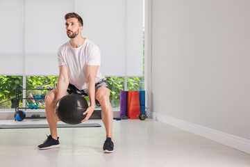 Fototapeta premium Muscular man doing squats with medicine ball in modern gym, space for text