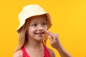 Fototapeta premium Mother applying sun protection cream onto her daughter's nose on yellow background, closeup