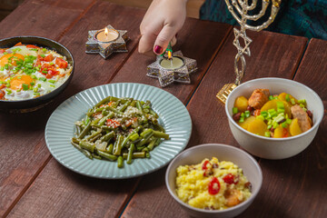A Jewish woman's hand lights Shabbat candles at the table.