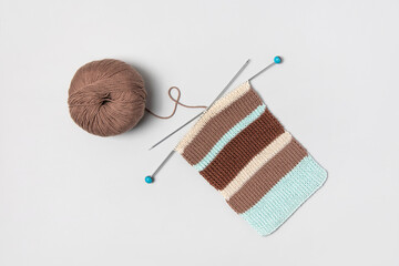 Brown beige and turquoise piece of striped knitting with knitting needles and ball of brown thread on gray background. Homemade needlework and knitting of warm, clothes and toys. Concept creativity