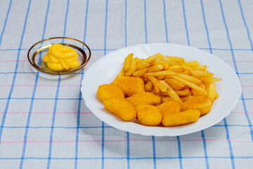 French fries and chicken crispy nuggets in a plate on a tablecloth