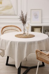 Table with white tablecloth, dried flowers in vases and chairs in stylish room. Interior design