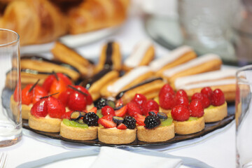 Assorted éclairs and fruit tartlets with berries on a serving plate