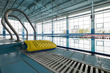 An indoor swimming pool with clear water features lane markers. A yellow and blue kickboard rests...