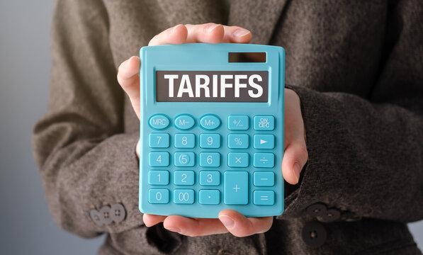 A person is holding a calculator with the word Tariffs on it