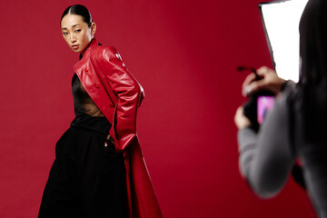 Fashion asian woman in red leather jacket and black pants taking a photo with a camera in front of...