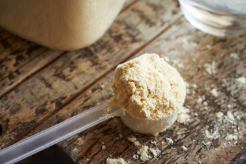 Whey protein powder in a measuring cup on a wooden table