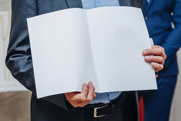 man in jacket holds blank sheet of paper in hands, copy space