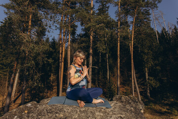 A woman meditating and practicing yoga on top of a rock at sunset, embracing wellness, mindfulness,...