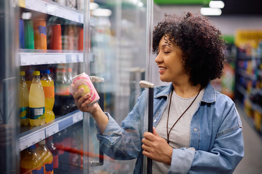 Happy woman taking soda at refrigerated section in supermarket.