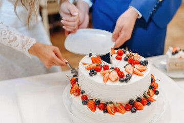 bride and groom cut white wedding cake, decorred with strawberries, wedding celebration