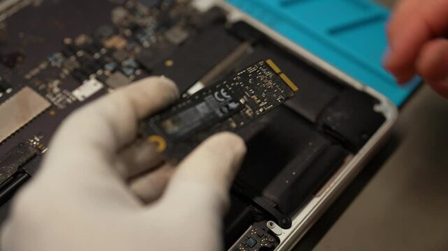Professional computer master holding solid state drive (ssd) above open laptop, during computer repair and upgrade process, close-up. Concept of computer hardware, repairing, upgrade and technology.