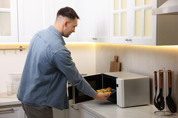 Man putting plate with lunch into microwave in kitchen