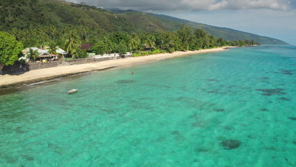 Aerial view of a tropical beach inviting tourists to swim in crystal clear turquoise water, a perfect vacation travel destination with lush vegetation and a cloudy sky