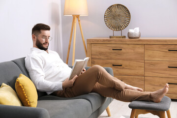 Handsome man with book relaxing on sofa at home