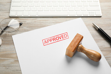 Sheet of paper with word Approved, stamp, keyboard and pen on white wooden table, closeup