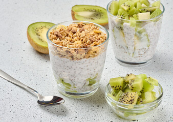 Glass filled with chia seed pudding, layered with diced kiwi at the bottom and topped with crunchy granola