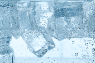 Refreshing soda water with ice cubes as background, closeup