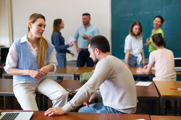 Young positive student is chatting with a fellow student girl in a university auditorium