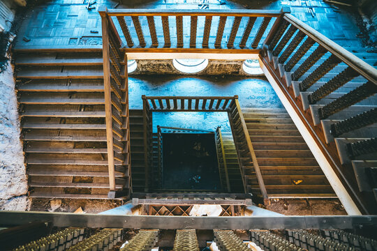 Top view of spiral staircase in abandoned building with ornate railing and circular windows, mysterious atmosphere of decaying structure. - Powered by Adobe