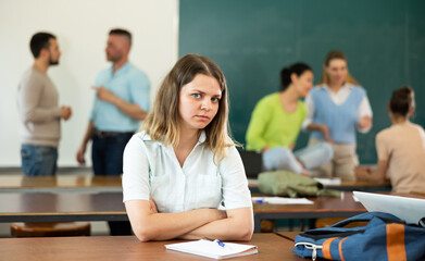 Upset girl sitting at table in auditorium during break on background with other students