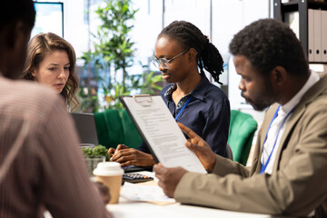 Naklejka premium Forecast affiliates collaborating in a high end workspace to determine resource allocation plan for project success, utilizing smart technology and infographics to present data driven insights.